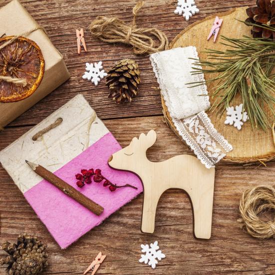 Træbord med juleting på, heriblandt et rensdyr i træ, en gave, kogler, tørrede appelsiner og små snefnug.