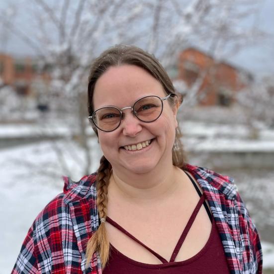 Bibliotekar Lisbeth Lohse Jørgensen. Hun smiler og er iført en rød bluse og skovmandsskjorte. Hun står udenfor, med sne i baggrunden.