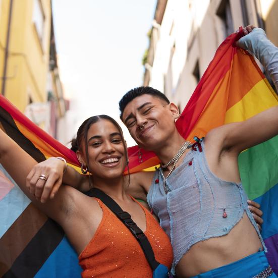 To personer, der holder om hinanden og er draperet i et Pride Progress-flag.