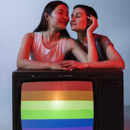 To kvinder, der læner sig ind over et tv med regnbueflag på.