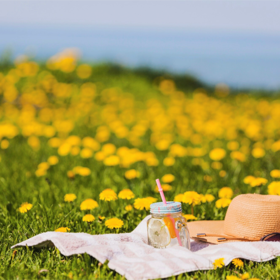 Solhat og en kold drink, der ligger på et tæppe ved stranden.