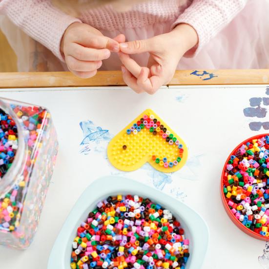 Et barn, der er ved at lave en perleplade formet som et hjerte.