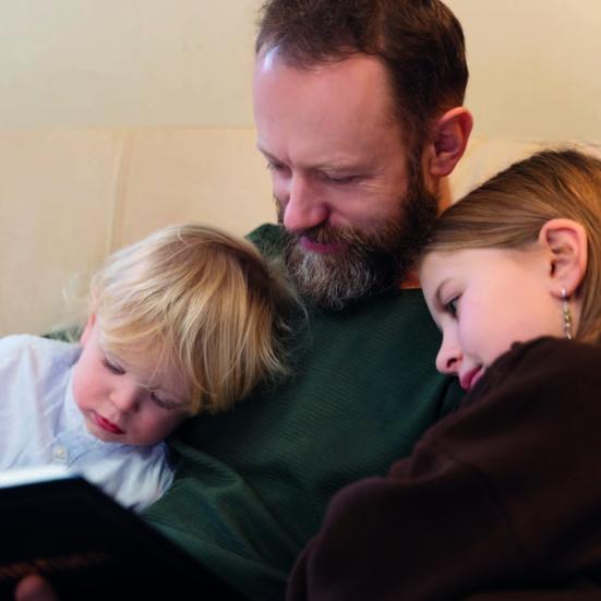 En mand, som læser en bog for to børn, der sidder op ad ham.