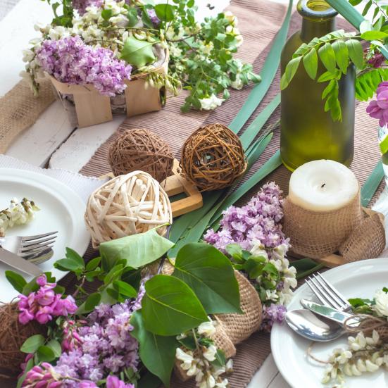 Opdækket bord med friske blomster, bloklys, vaser, bestik og pynt.