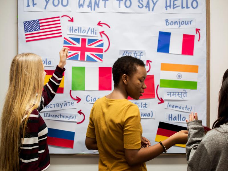 Tre kvinder står foran en tavle med en masse flag på, samt teksten "If you want to say hello".