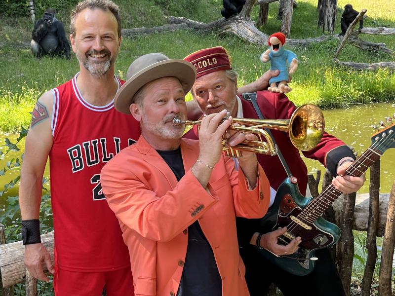Et orkester bestående af tre mænd i rødligt tøj. Den forreste mand spiller på trompet og har en hat på.