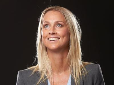 Portrætfoto af Camilla Martin, der smiler. Hun er iført en grå blazer, og kigger opad mod venstre hjørne.