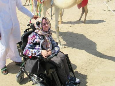Anna i elektrisk kørestol med kamel i baggrunden