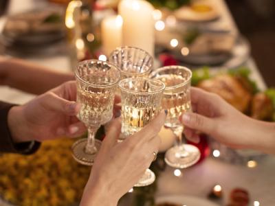 Fire hænder, der skåler med hvidvin over et middagsbord.
