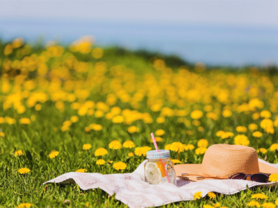 Solhat og en kold drink, der ligger på et tæppe ved stranden.