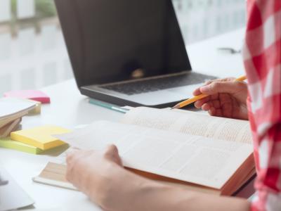 En kvinde, der læser i en bog. Ved siden af hende ses en computer og forskellige studieredskaber.