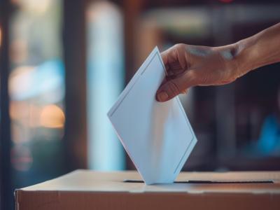 Person, der putter et stykke papir ned i en lukket kasse - de stemmer til valg.