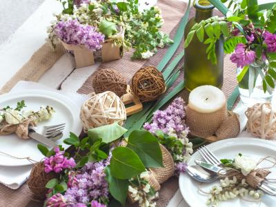Opdækket bord med friske blomster, bloklys, vaser, bestik og pynt.