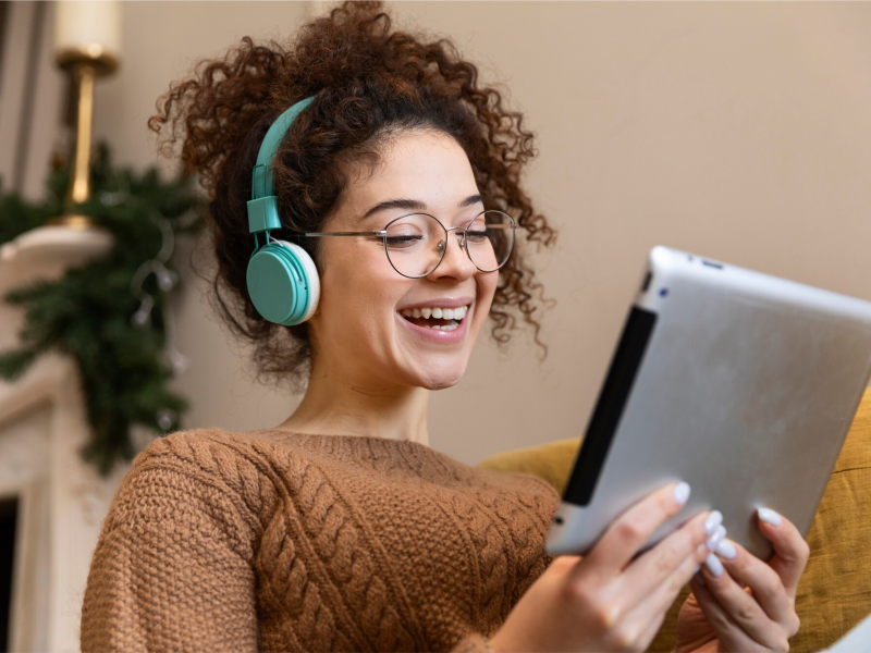 Kvinde med høretelefoner på, der smiler mens hun læser noget på en tablet.