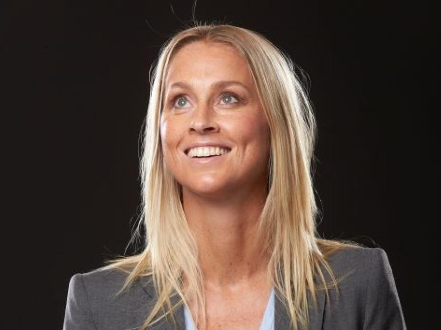 Portrætfoto af Camilla Martin, der smiler. Hun er iført en grå blazer, og kigger opad mod venstre hjørne.