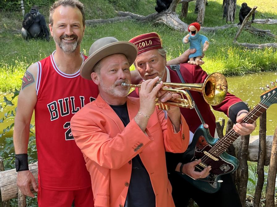 Et orkester bestående af tre mænd i rødligt tøj. Den forreste mand spiller på trompet og har en hat på. 