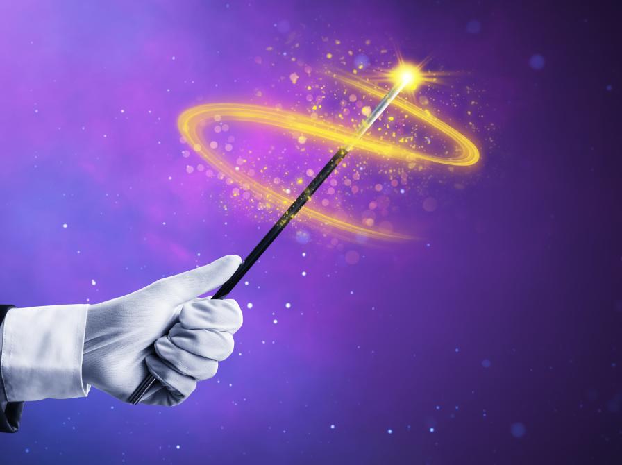 Hånd, der svinger en tryllestav med gnister og glimt foran en lilla baggrund.